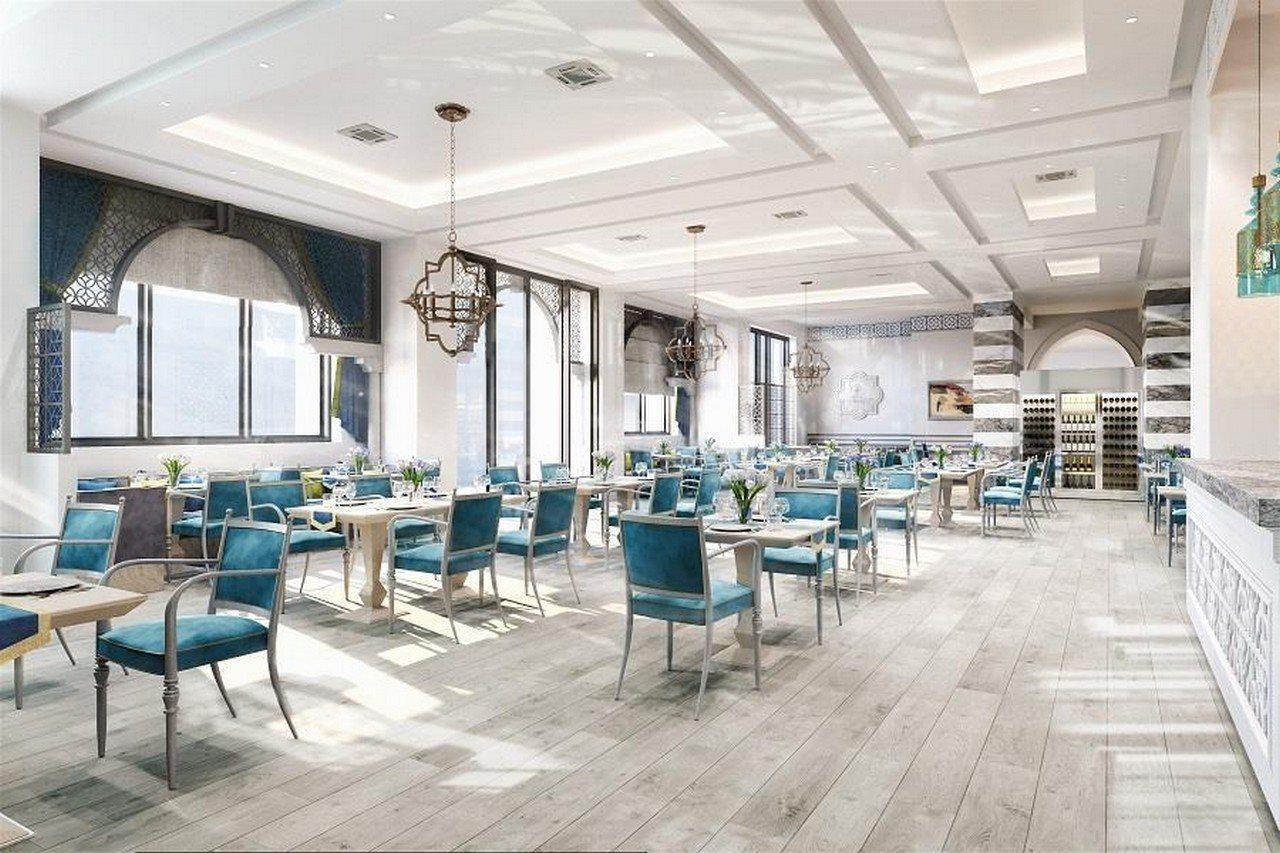 Grand Swiss-Belhotel Waterfront Seef Sanabis Exterior photo The image depicts a modern dining area with a bright and airy atmosphere. It features numerous tables and chairs arranged throughout the space. The tables are set with simple, elegant decor, and the chairs are upholstered in a vibrant blue fabric. La