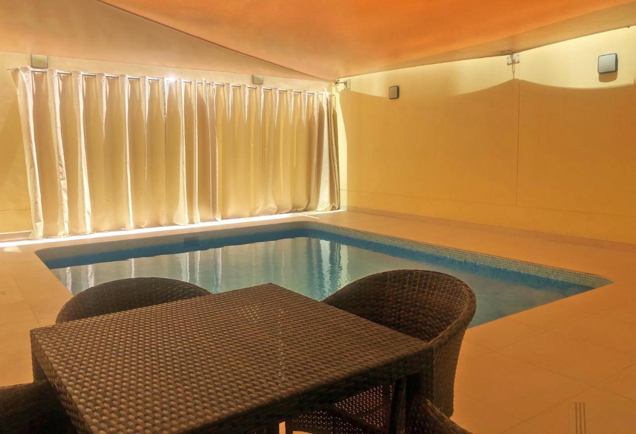 Grand Swiss-Belhotel Waterfront Seef Sanabis Exterior photo The photo shows an indoor area featuring a small swimming pool surrounded by walls. To one side, there are sheer curtains that allow light to filter in. There is also a small table and two chairs made of wicker, positioned close to the pool, creating